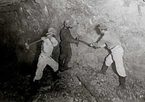 A photo of three miners drilling a hole in a mine.
